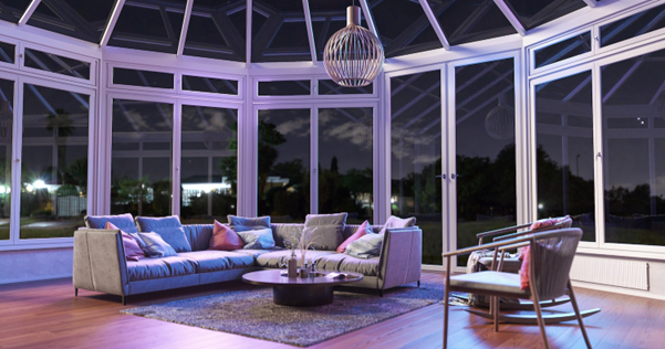 A white solarium with some chairs, a table, and a couch under a suspended light fixture inside a solarium with the nighttime sky outside.